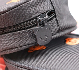 Detailed close-up of a bear-shaped metal zipper pull on a black nylon pencil case