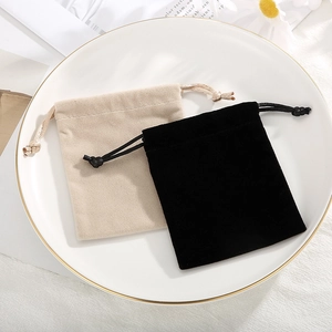 Minimalistische Kordelzug-Samtbeutel für Schmuck in Schwarz und Beige auf weißem Teller
