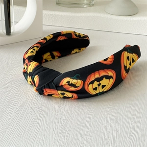 Détail d'un serre-tête d'Halloween noué avec des motifs citrouilles sur tissu noir