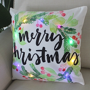 White Merry Christmas LED pillow with festive wreath on sofa, warm glowing home decor