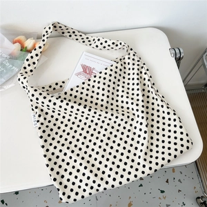 Detail of beige canvas tote bag with black polka dots on a minimalist white desk