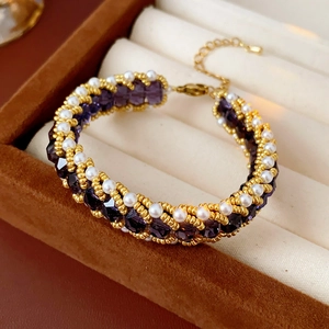 Detailed shot of purple crystal and pearl woven bracelet on dark suede jewelry box