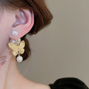 Macro view of gold butterfly earrings with faux pearls on a model for French vintage style