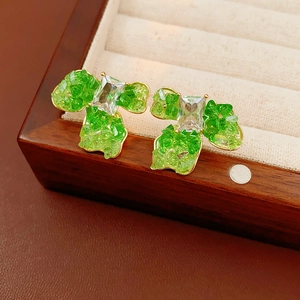 Detail of flower earrings with green stones and clear crystal on a wooden jewelry box
