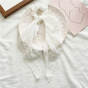 Detail view of white pleated hair scrunchie with long ribbon on decorative ceramic plate