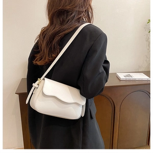 Chic white leather crossbody bag with curved flap and gold hardware on elegant model