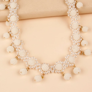 Close-up of woven pearl flower belt with gold metal accents on a pink background