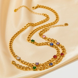 Collier en acier doré avec zircons ronds multicolores posé sur un tissu en soie dorée
