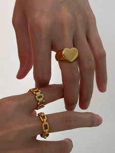Detailed view of three chunky gold heart and chain rings worn on hands for a retro look