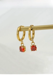 Detail of gold titanium steel hoop earrings with round red zircon stone pendant
