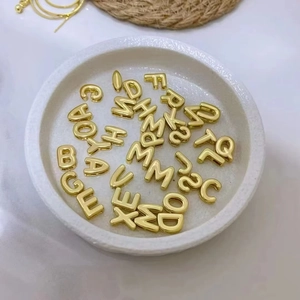 Golden DIY alphabet charms in a white dish, minimalist composition for jewelry making