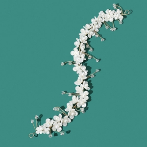 Bridal hairpiece with white flowers, pearls and crystals on gold wire over green background