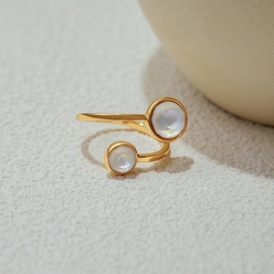 Close-up of golden open ring featuring two round iridescent stones on a jewelry stand