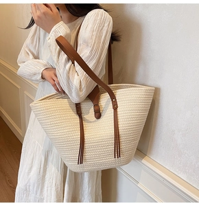 Detail of woven beige tote bag with brown leather straps and tassels on model