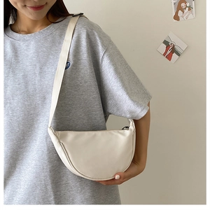 Detail of white nylon crescent crossbody bag with wide shoulder strap worn by a person