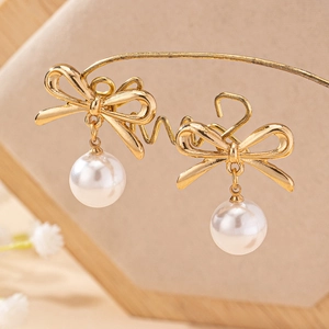 Elegant gold bow earrings with white pearl pendants displayed on a jewelry stand