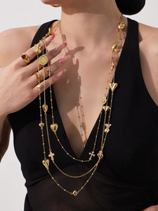 Detail van gelaagde gouden lange ketting met hart-, kruis- en beerbedeltjes op model
