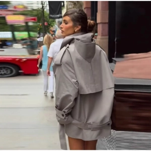 Back view of a loose grey hooded trench coat with belt and storm flap on city street