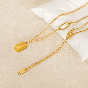 K18 gold plated stainless steel necklace with gold bar pendant on a textured backdrop