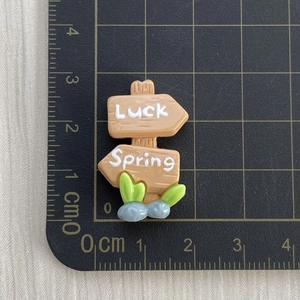 Macro shot of 3.5cm resin wooden signpost figurine with Luck and Spring text on grid mat