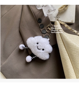 Close-up of fluffy white plush smile pendant with striped legs on beige textured bag