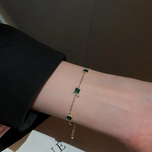 Gros plan d'un bracelet doré avec pierres émeraude carrées porté au poignet