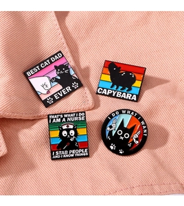 Enamel pins featuring black cat and capybara designs displayed on pink fabric