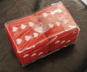 Close-up of red plush car dice with white heart embroidery in clear plastic packaging