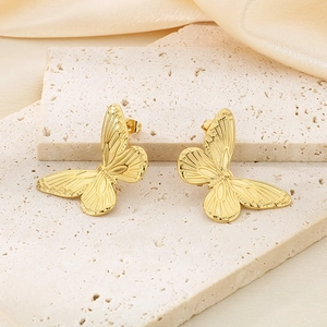 Detailed view of golden butterfly earrings with textured wings on a stone and silk background