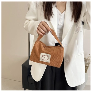 Close-up of brown corduroy handbag with cute cartoon bear label and soft fabric texture