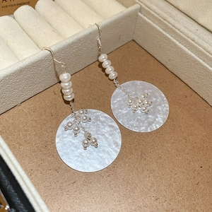 Detail view of pearl hook earrings with a shimmering round mother-of-pearl pendant disk