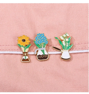 Detailed close-up of three floral coffee cup enamel pins pinned on pink fabric texture