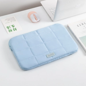 Close-up of light blue quilted laptop sleeve with grid stitching on a tidy desk