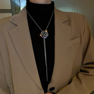 Détail d'un long collier argenté avec pendentif camélia sur un blazer beige