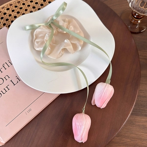 Detail of tulip scrunchie with green ribbons and pink flower buds on a ceramic plate