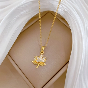 Close-up of golden maple leaf necklace with sparkling crystals in a beige jewelry box