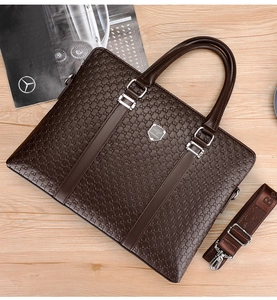 Detailed view of brown leather briefcase with embossed patterns and logo on wooden surface