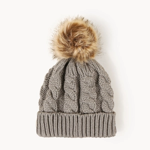 Detail of grey cable knit winter hat with a fluffy faux fur pompom and ribbed cuff