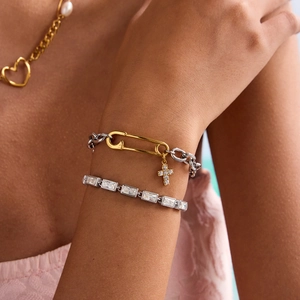 Detail of silver cubic zirconia tennis bracelet and gold cross charm jewelry on a model