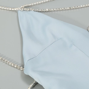 Detail of light blue satin fabric with sparkling rhinestone chain straps on a grey background