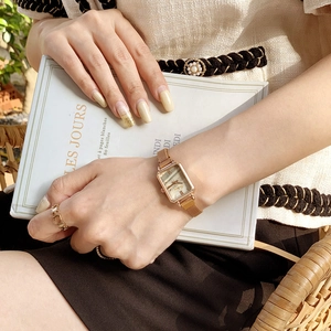 Detail shot of a minimalist rose gold rectangular watch on a wrist against a book