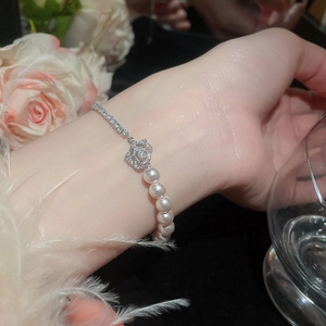 Detailed shot of a French pearl bracelet with a zircon rose charm worn on a wrist