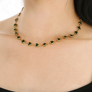 Detail of a gold heart link necklace with dark green gemstones worn by a model
