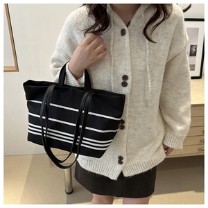 Macro shot of large black canvas tote bag with white stripes and slim leather straps
