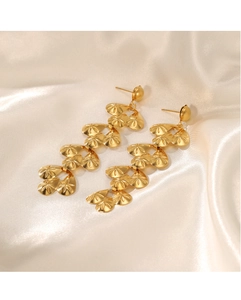 Detail of long gold drop earrings with textured heart charms on elegant beige silk fabric
