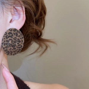 Close-up of a model wearing a large round leopard print earring with a soft velvet texture