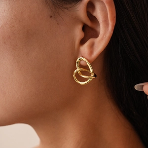 Primo piano di orecchini a cuore irregolari placcati oro 18k con texture metallica