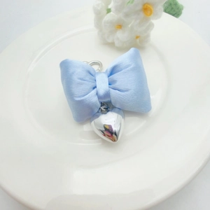 Detail of light blue ribbon bow and silver heart pendant keychain on a white plate