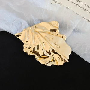 Macro shot of large polished gold leaf brooch featuring creative pleated metal texture