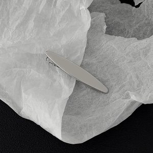 Detail of a sleek silver streamlined metal hair clip on artistic paper and leather background